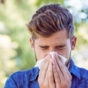 Man sneezing into tissue outdoors