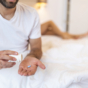 Man holding blue pill sitting on edge of bed